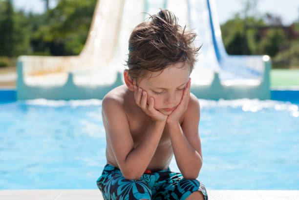 sad little boy sitting near water pool in summer resort water park